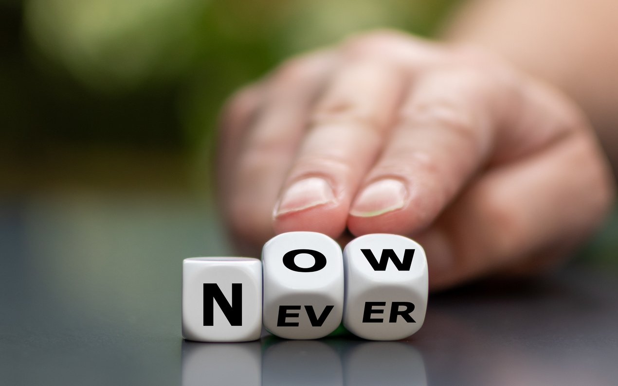 Now or never? Hand turns dice and changes the word "never" to "now".